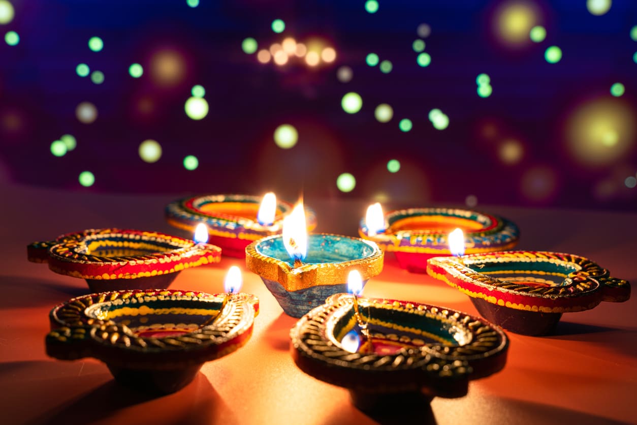 A circle of vibrant, hand-painted oil lamps lit against a festive background, capturing the warmth and radiance of Deepavali.