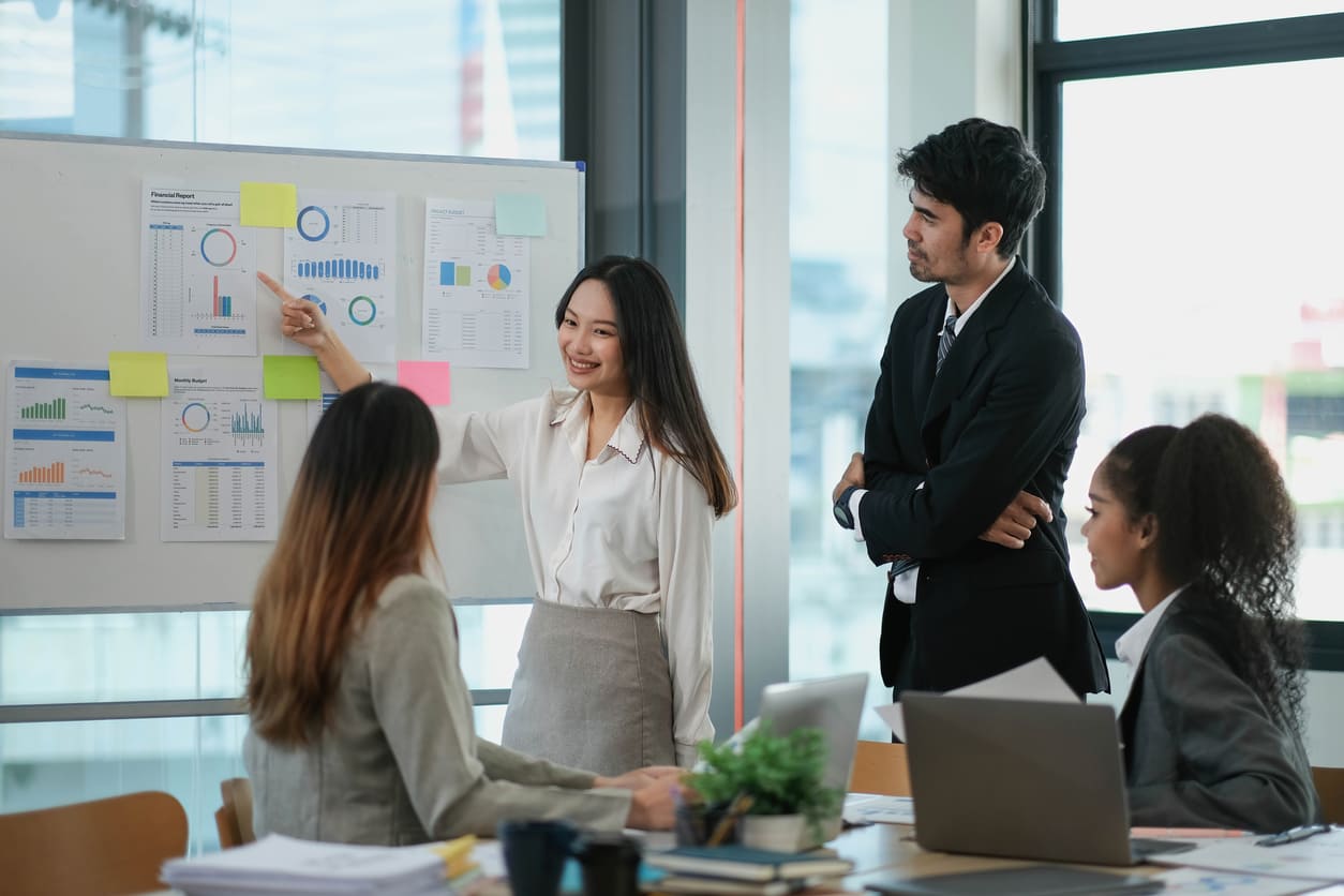 A woman confidently presenting data to a diverse group of colleagues in a modern office, symbolizing leadership and inclusion.