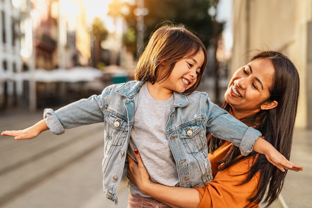 A smiling mother holding her happy child outdoors, capturing a warm and playful moment filled with love and connection.