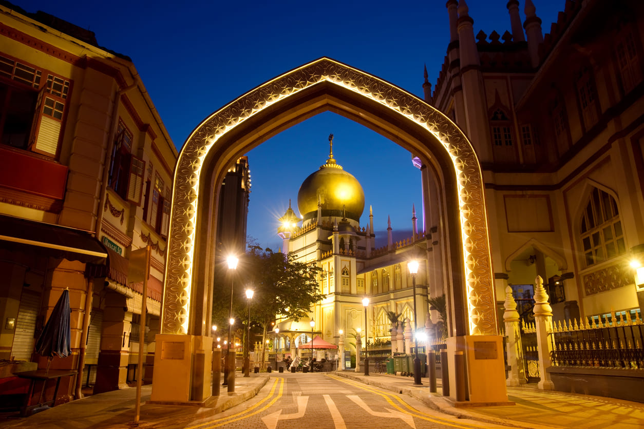 The iconic Sultan Mosque in Singapore illuminated at dusk, framed by a decorative archway, reflecting the serene and spiritual atmosphere of Ramadan.