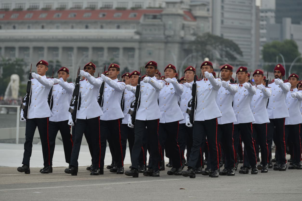 SAF personnel marching in synchronized formation during a ceremonial parade, with city landmarks in the background, symbolizing national pride and military precision.