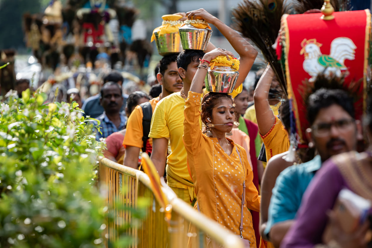 Devotees dressed in vibrant clothing walk in a Thaipusam procession, carrying decorated milk pots on their heads as an act of devotion.