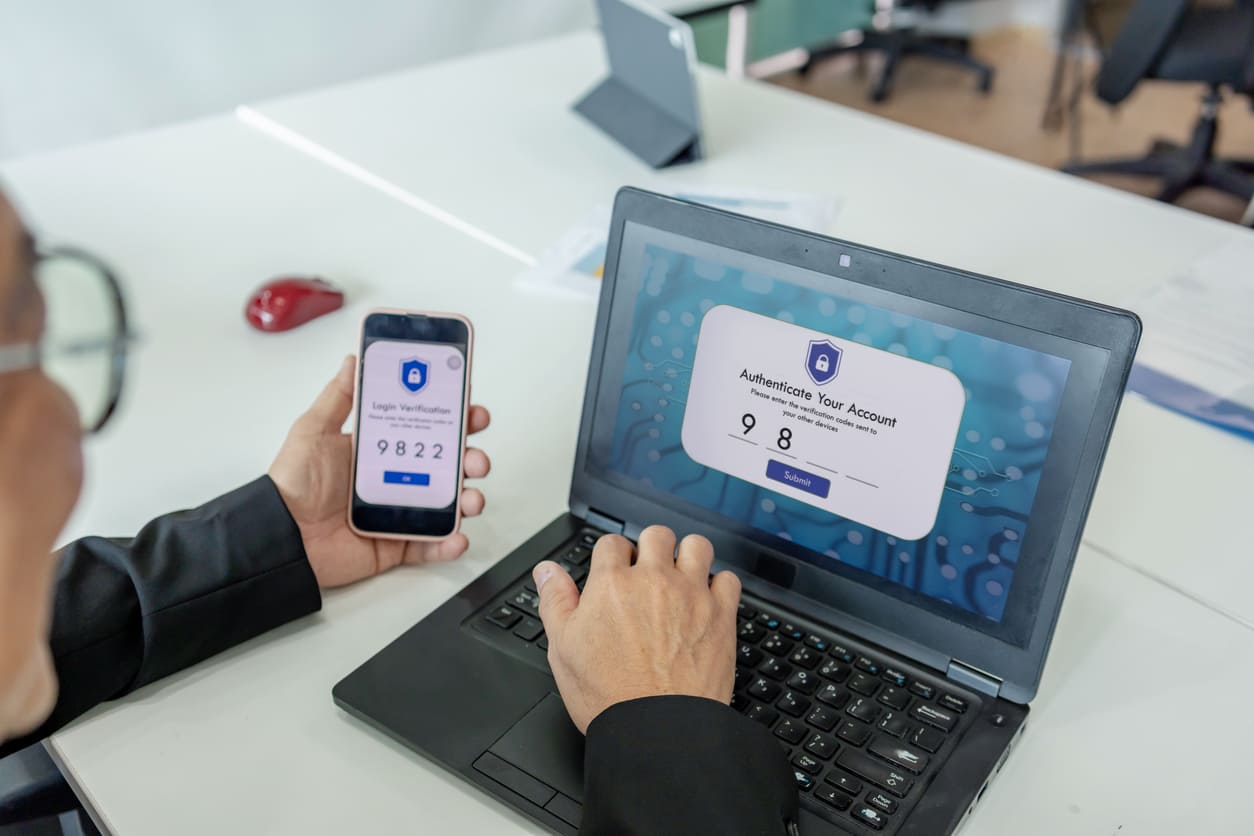 A person using two-factor authentication on a laptop and smartphone, demonstrating a key aspect of Digital Defense in today's cyber landscape.