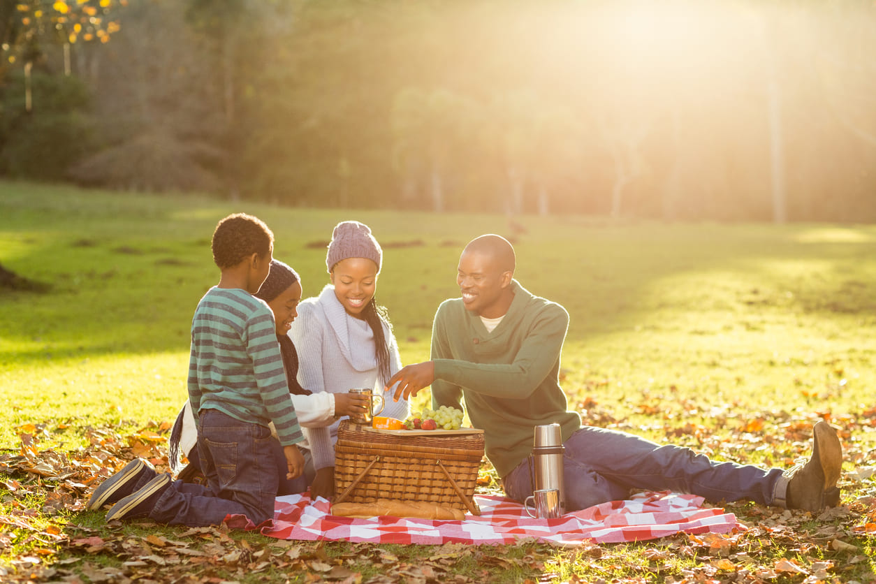 A cheerful family gathered on a picnic blanket in a sunny park, sharing food and enjoying quality time together.