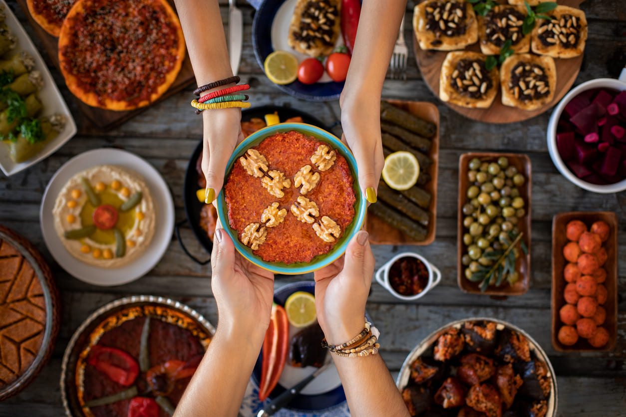 A vibrant table filled with traditional dishes, with hands exchanging a bowl of food, symbolizing sharing and celebration during Eid al-Fitr.