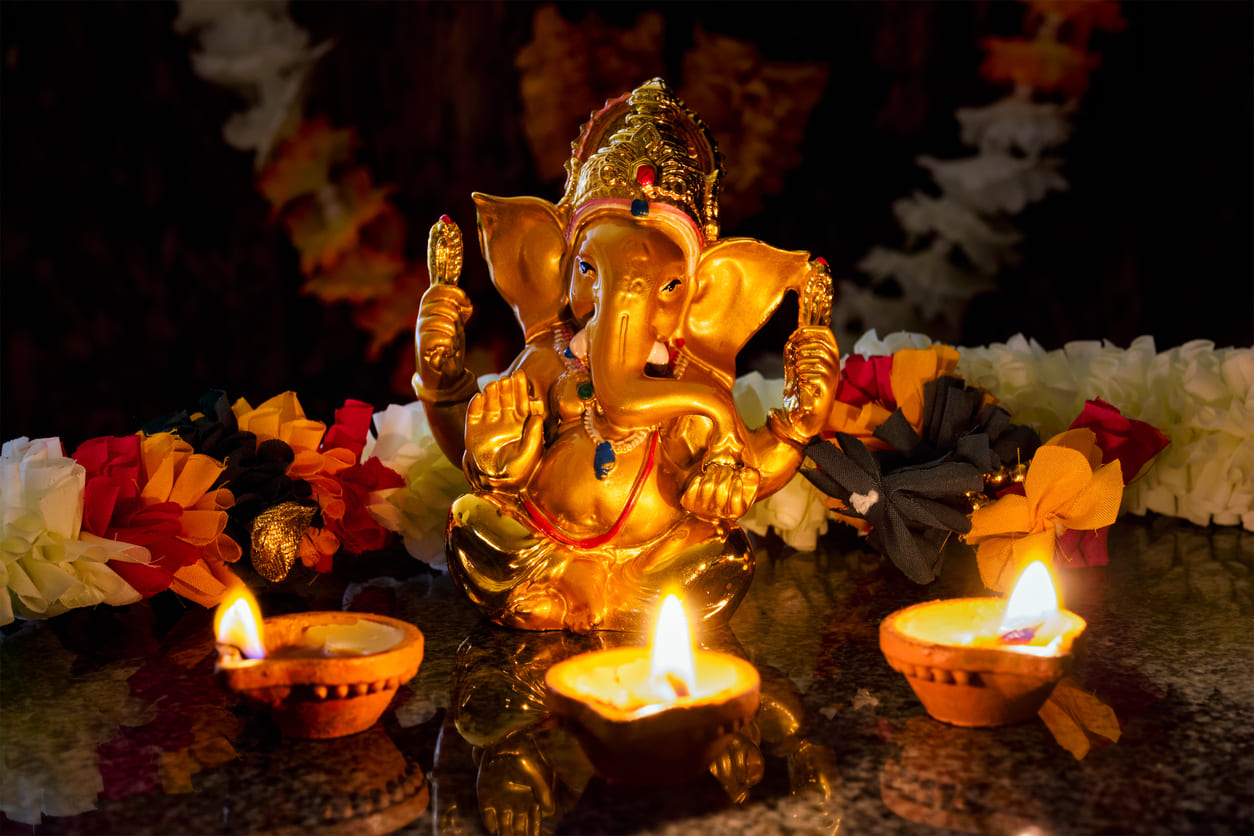 A golden idol of Lord Ganesha sits adorned with garlands and surrounded by glowing oil lamps, radiating festive warmth and devotion.