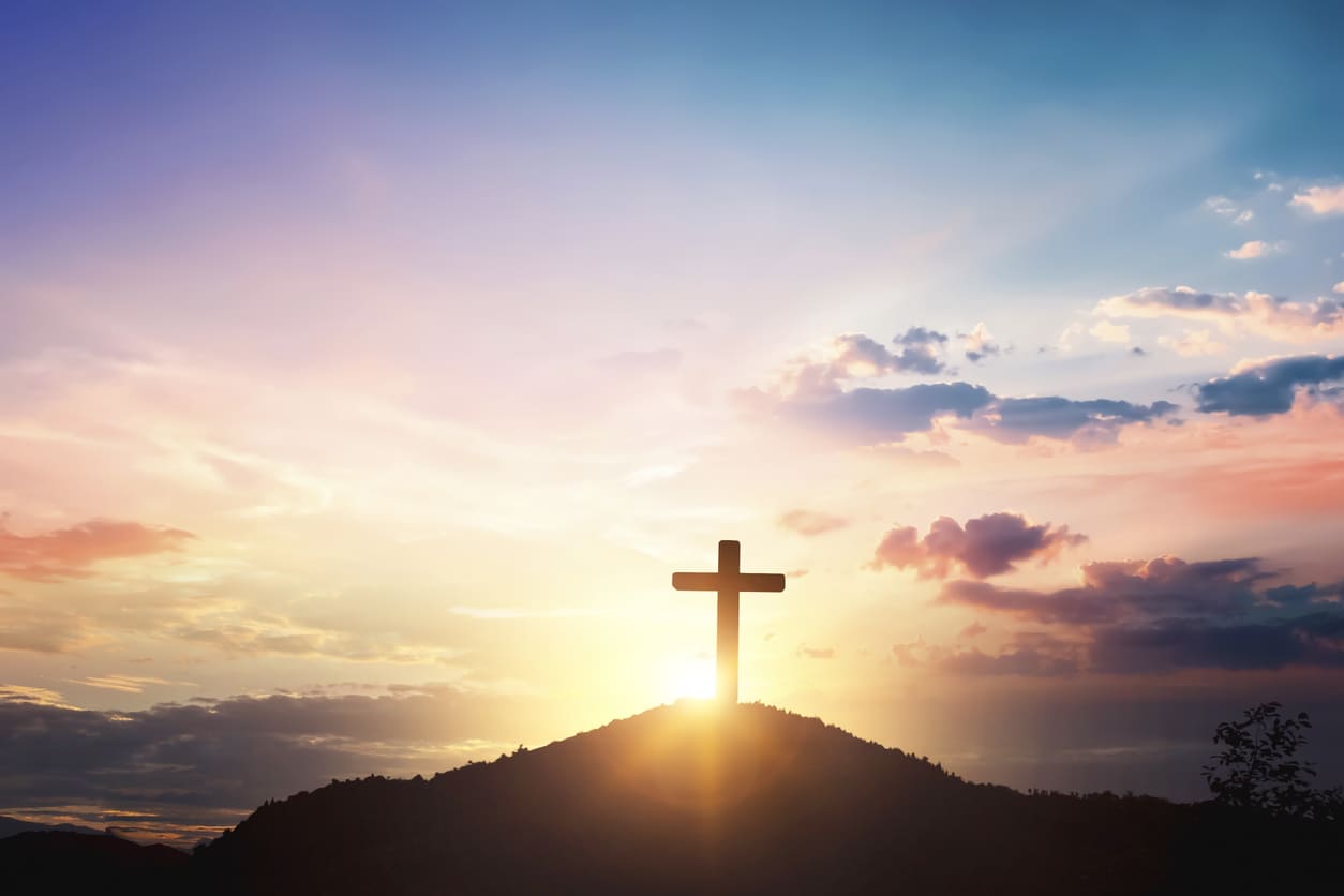 A cross standing on a hilltop, silhouetted against a peaceful sunrise sky, evoking reflection and reverence.