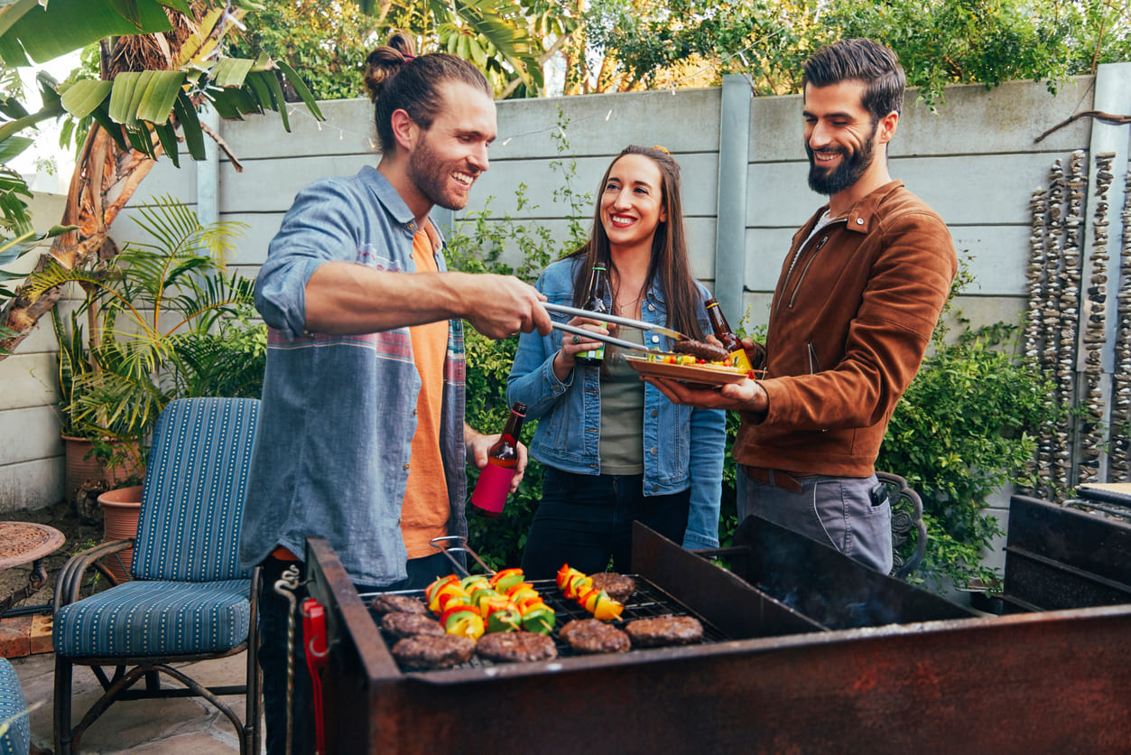 Friends smiling and enjoying a braai in a backyard setting, sharing food and celebrating together in a relaxed and festive atmosphere.