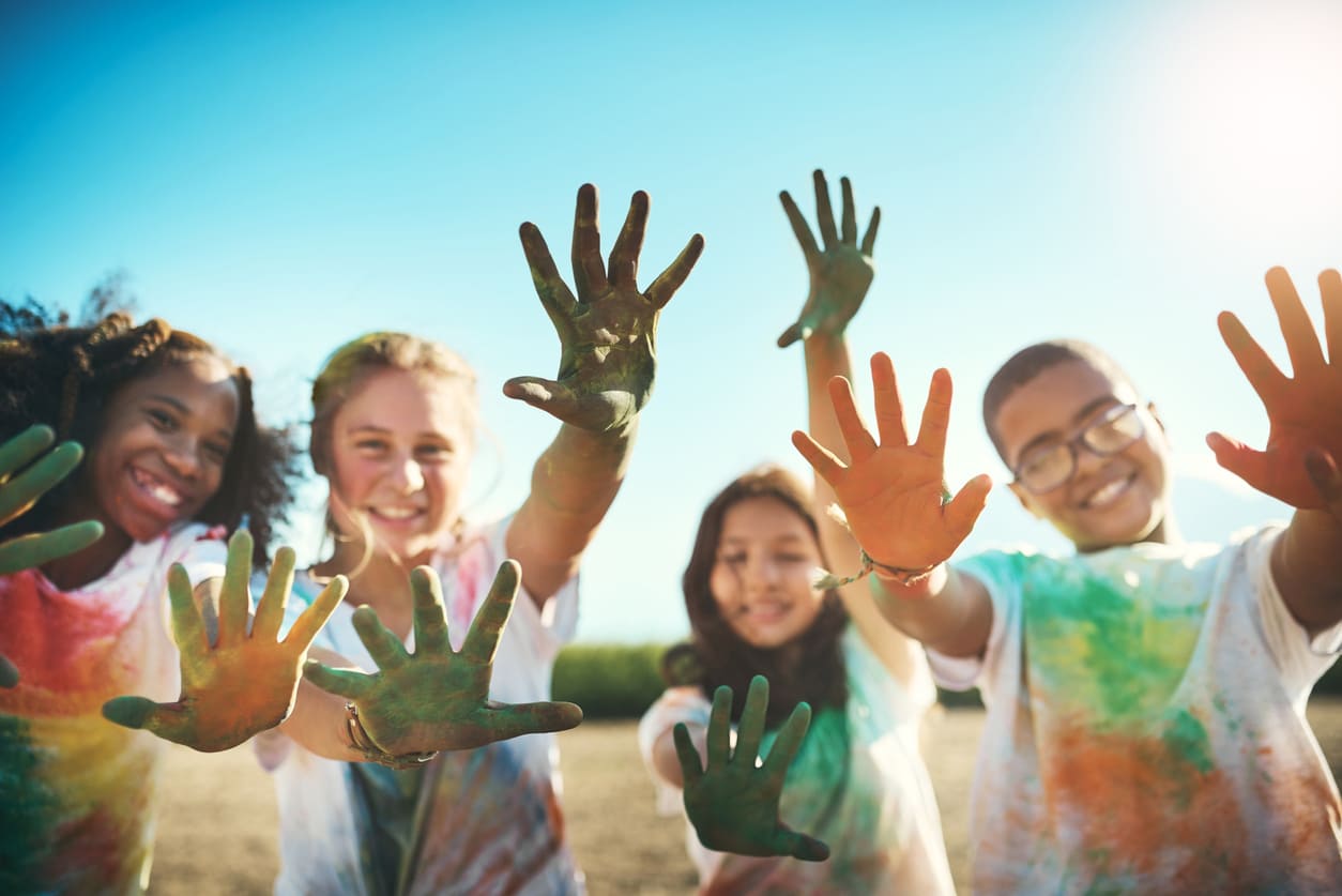 A cheerful group of children with colorful hands smiles brightly under the sun, enjoying the festive celebration of Holi.