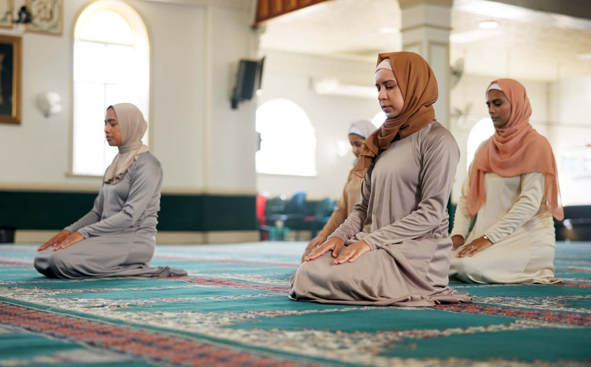 A group of Muslim women sit in calm prayer inside a mosque, reflecting the peaceful observance of Muharram.
