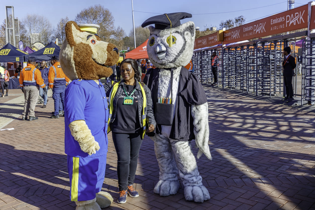 Cheerful team mascots posing at Emirates Stadium, ready to take part in a community cleanup for Nelson Mandela Day in Johannesburg.