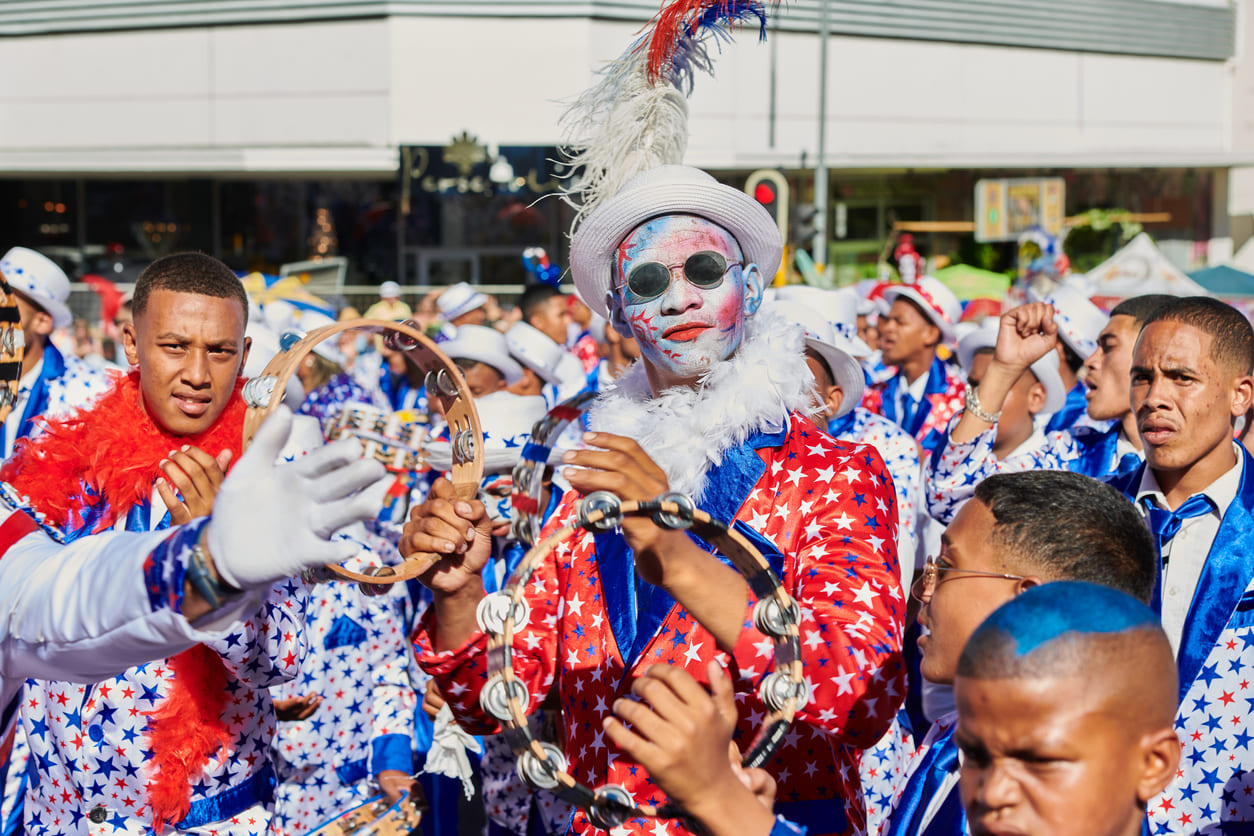 A vibrant minstrel troupe in colorful star-patterned costumes and painted faces, parading through Cape Town with tambourines and festive energy.