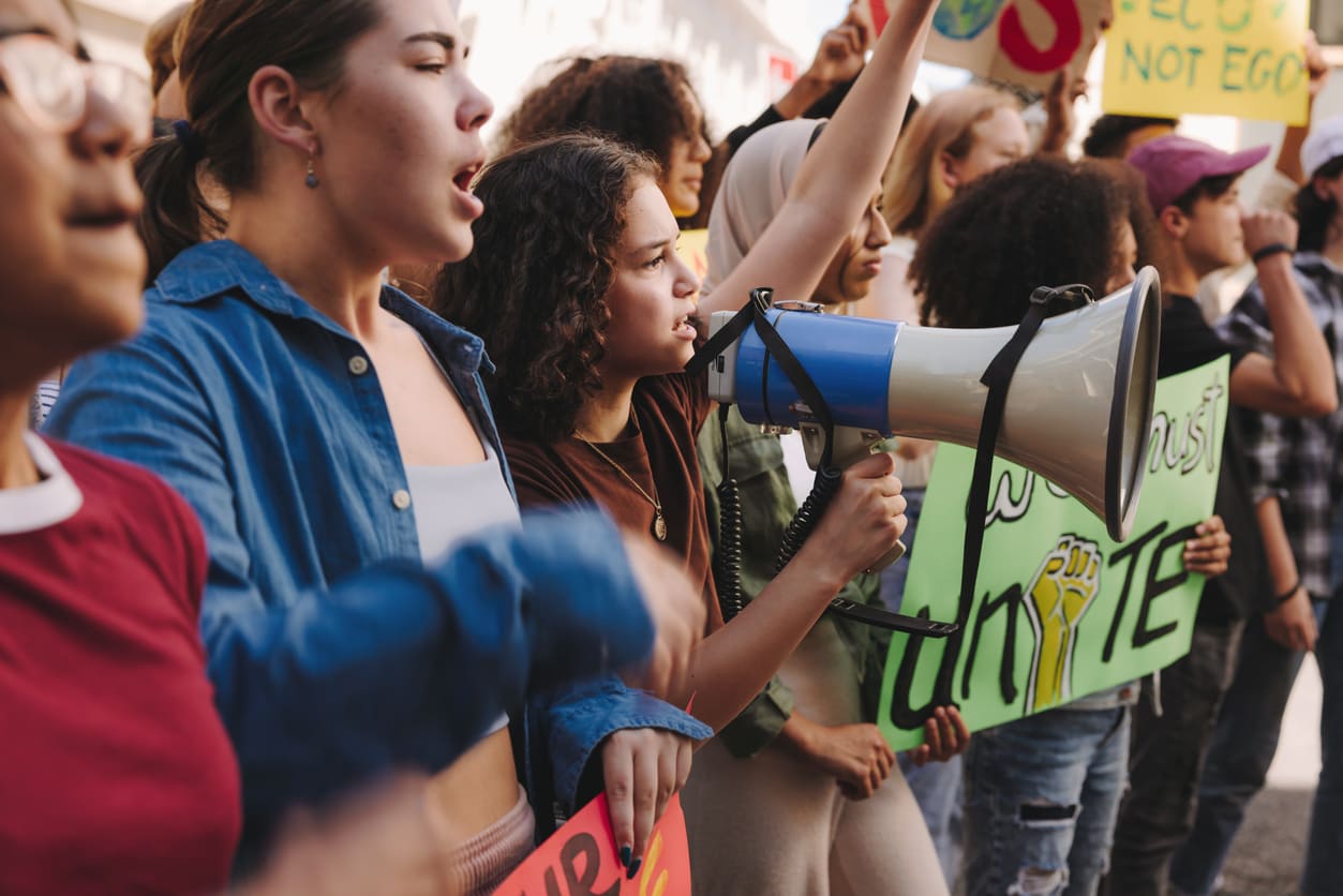 A diverse group of protesters holding signs and a megaphone, passionately calling for unity and workers' rights during a public rally.