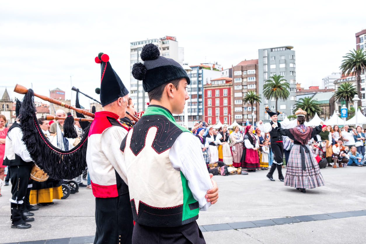 A vibrant scene of musicians playing traditional Cantabrian bagpipes and dancers in regional attire performing folk dances before an engaged crowd.