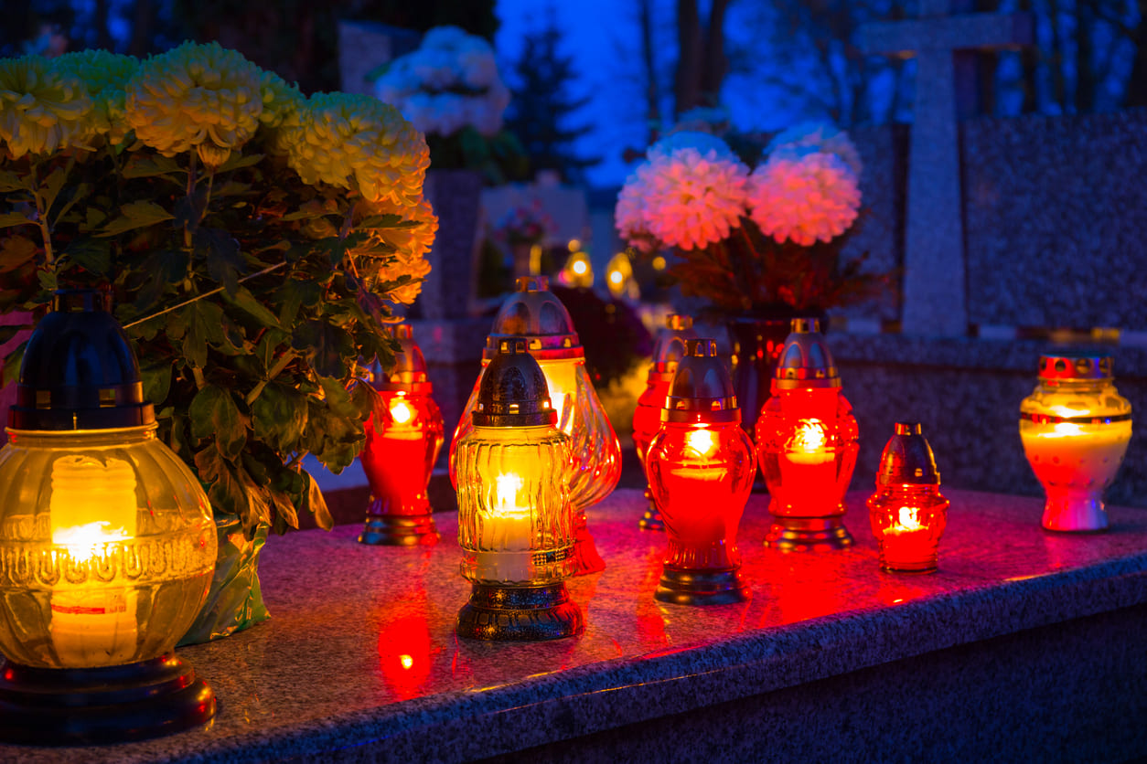 A row of glowing lanterns and fresh flowers placed on gravestones, creating a peaceful and respectful scene in a Swedish cemetery at dusk.