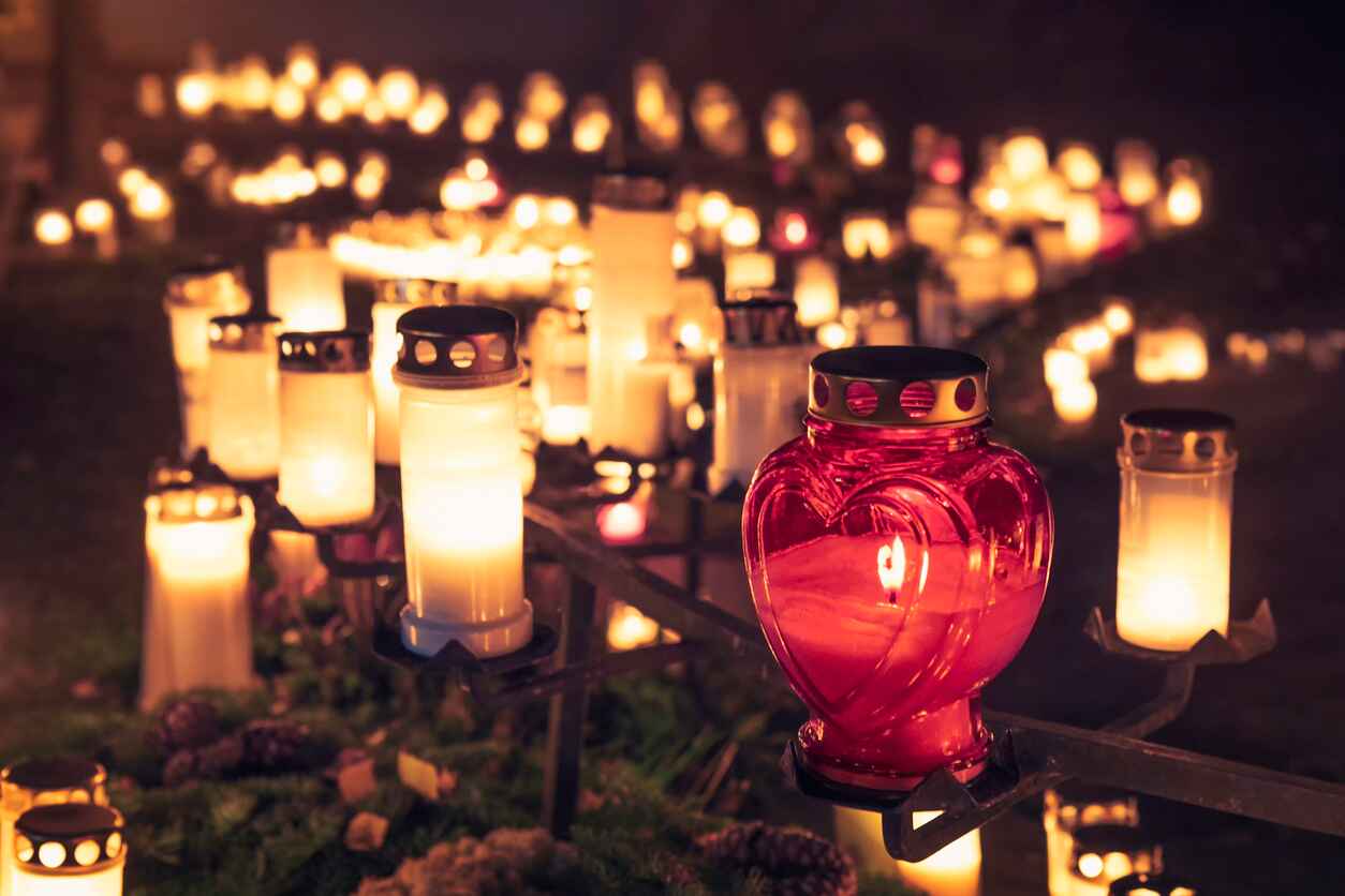 A cemetery illuminated by rows of glowing candles, with a red heart-shaped lantern in focus, symbolizing remembrance on All Saints' Eve.