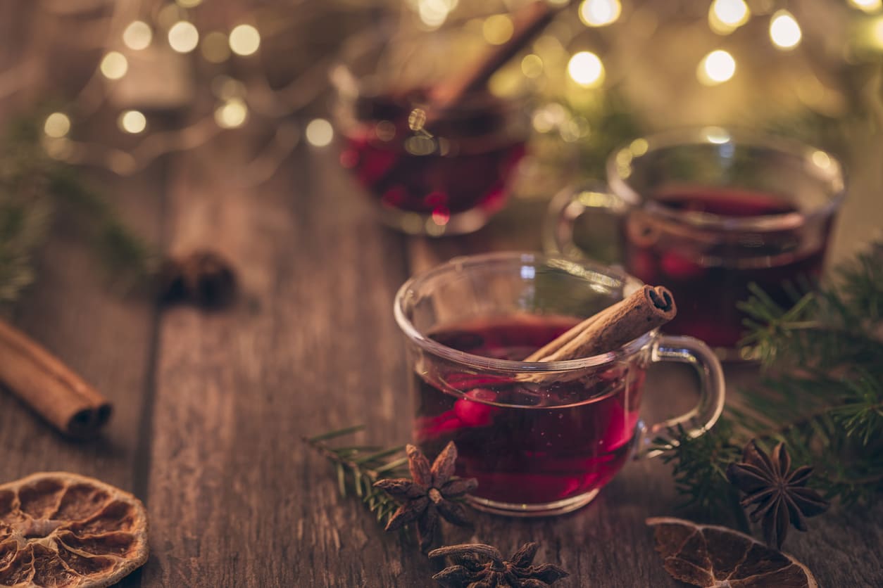 Cups of Scandinavian glögg with cinnamon sticks, surrounded by festive lights, dried citrus, and holiday greenery on a rustic wooden table.