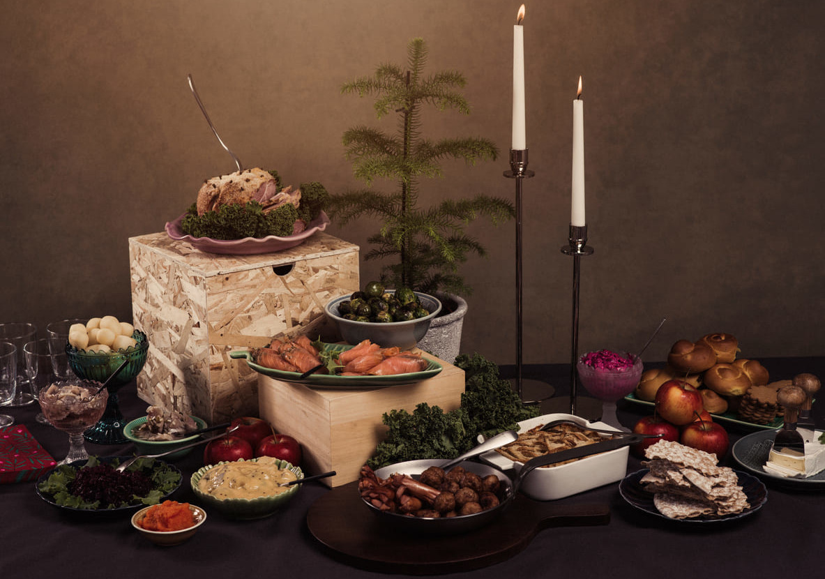 A beautifully arranged Swedish Christmas Eve julbord with traditional dishes, candles, and seasonal decorations creating a cozy festive setting.