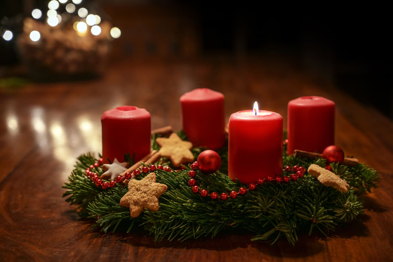 A festive Advent wreath with four red candles, one lit, surrounded by cookies and ornaments, capturing the warmth of First Advent Sunday in Sweden.