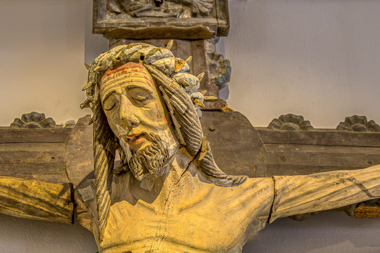 A close-up of an aged wooden sculpture of Jesus on the cross, showing detailed craftsmanship and evoking the solemn tone of Good Friday in Sweden.