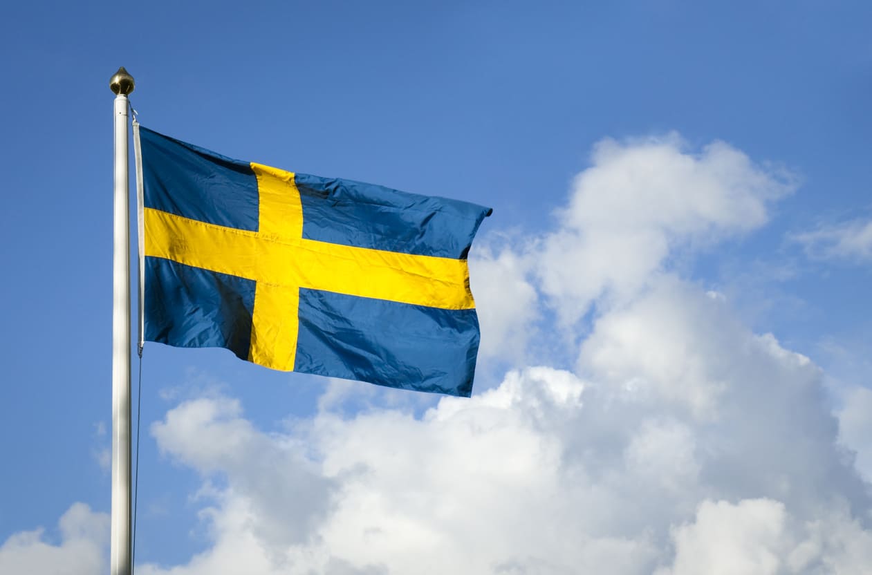 The Swedish flag fluttering against a bright blue sky with soft clouds, reflecting the spirit of National Day.