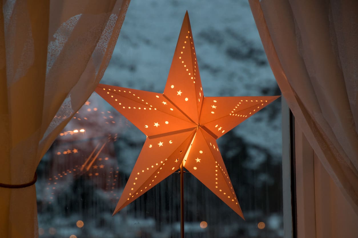 A softly lit paper star lantern glowing in a window, with snow-covered scenery visible outside, symbolizing the peaceful end of the Swedish Christmas season.