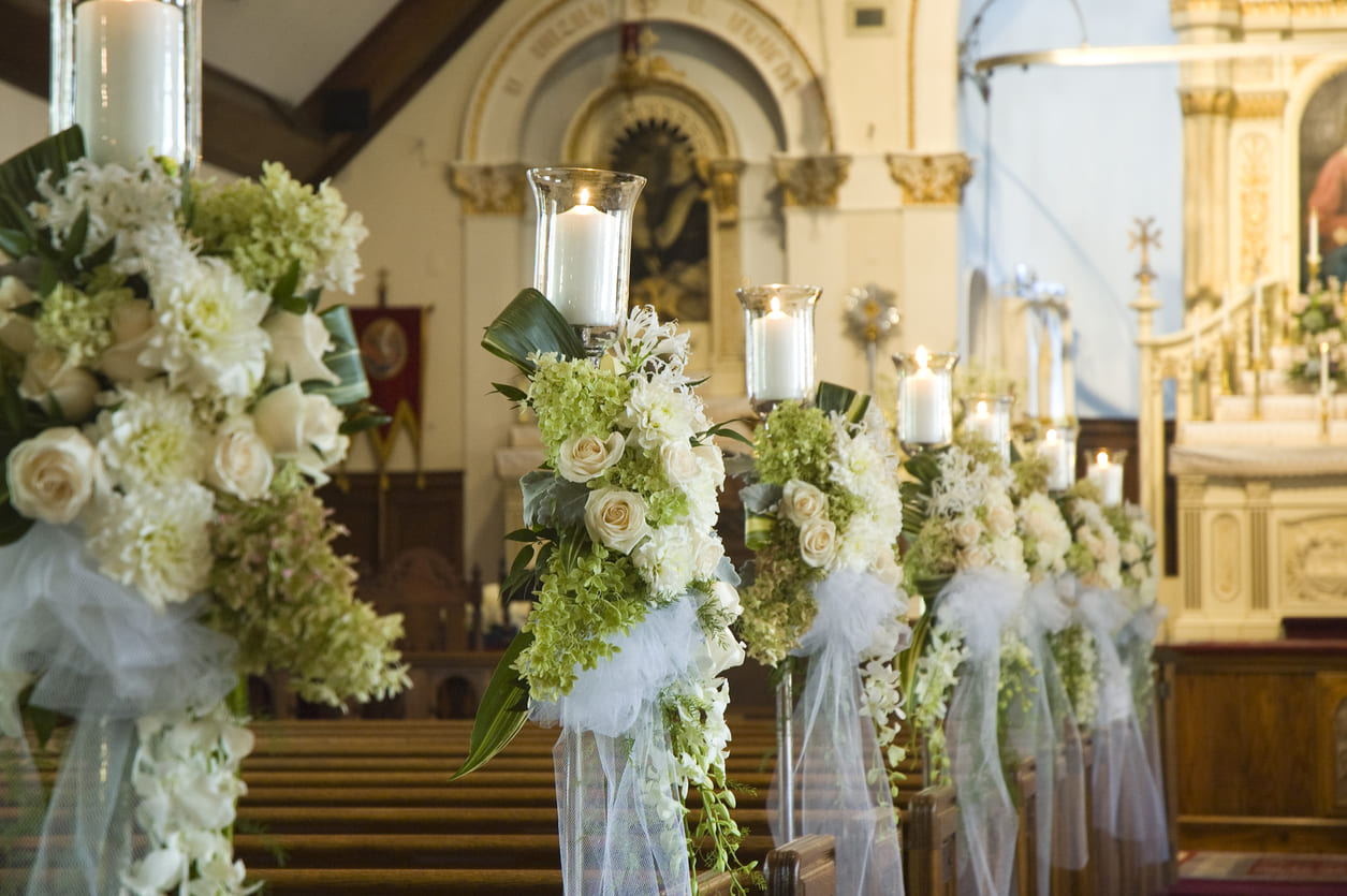 A church interior beautifully decorated with white flowers and candles along the pews, creating an elegant and serene wedding atmosphere.