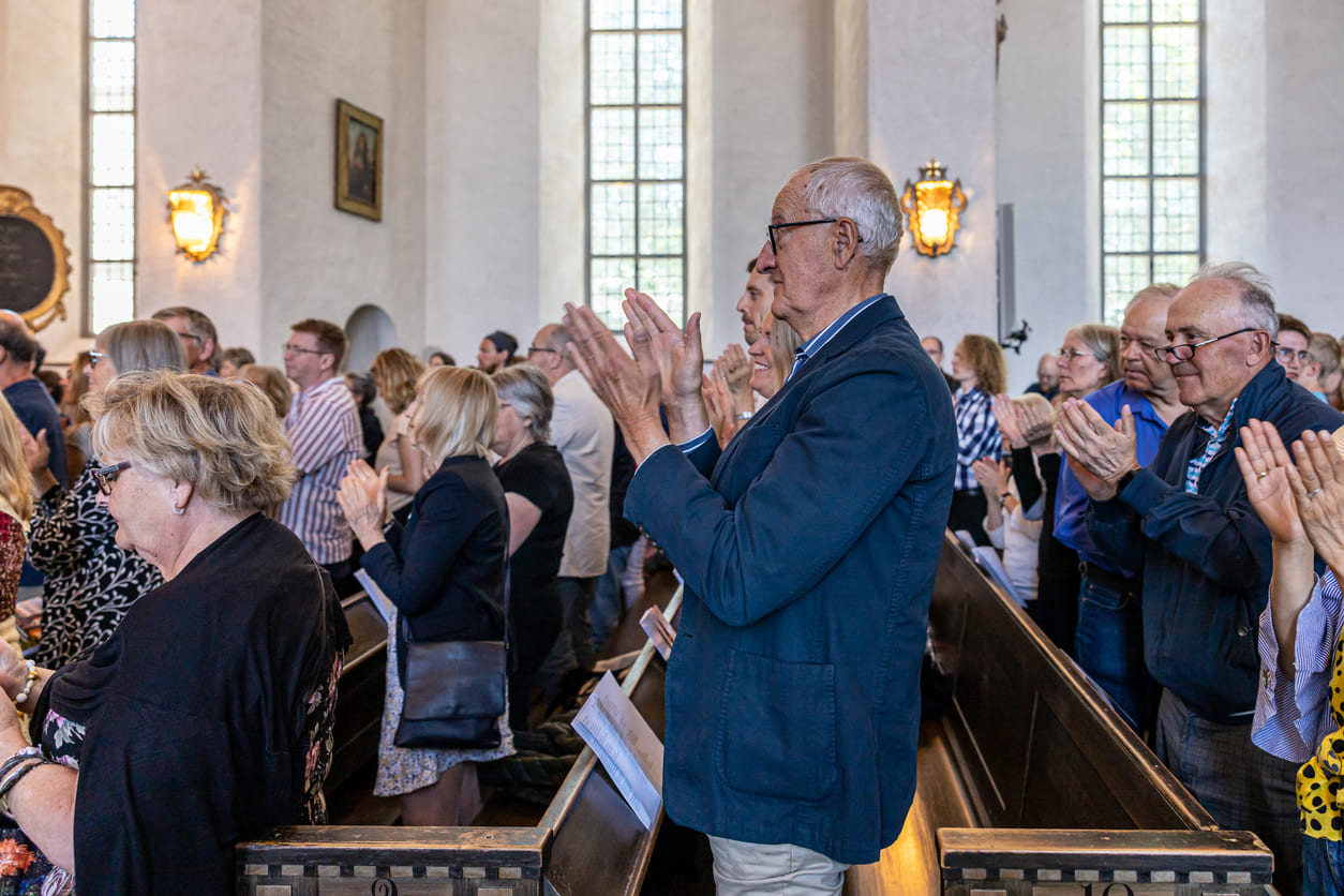 A lively congregation standing and applauding inside a bright Swedish church during a Whit Sunday service.