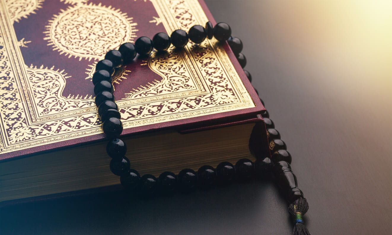 A beautifully adorned Quran with black prayer beads resting on it, reflecting devotion and spiritual focus.