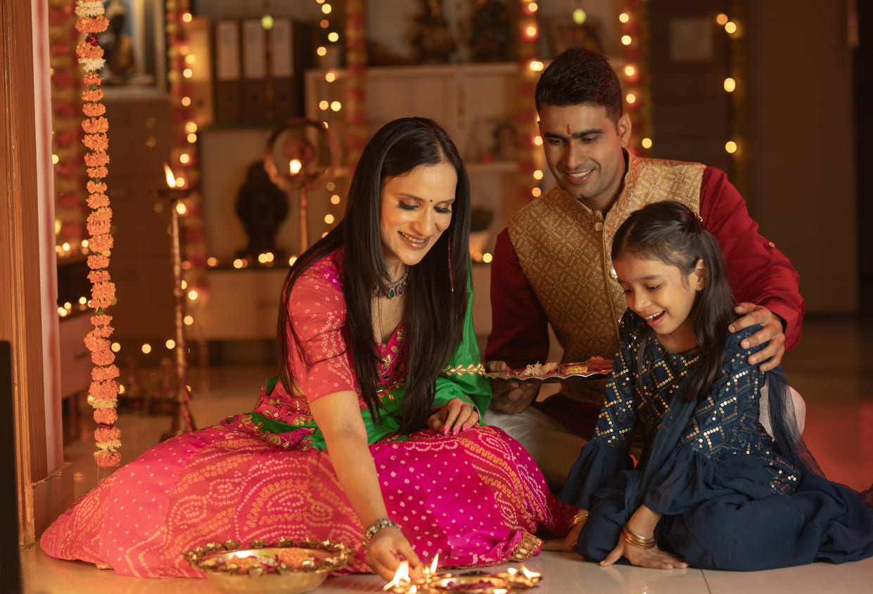 Family celebrating Diwali by lighting diyas, dressed in traditional attire, with festive decorations.