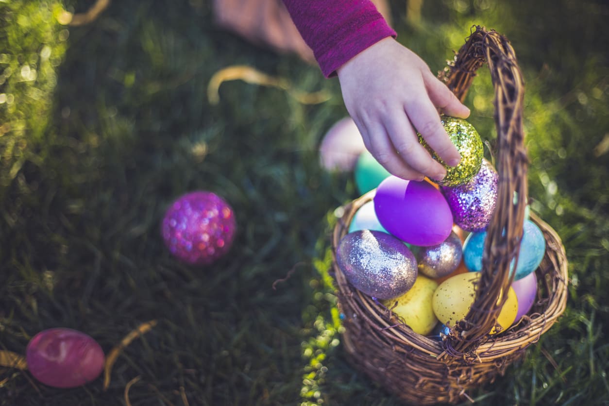 A child reaches into a basket filled with colorful, glittering Easter eggs, capturing the festive spirit of an Easter egg hunt.